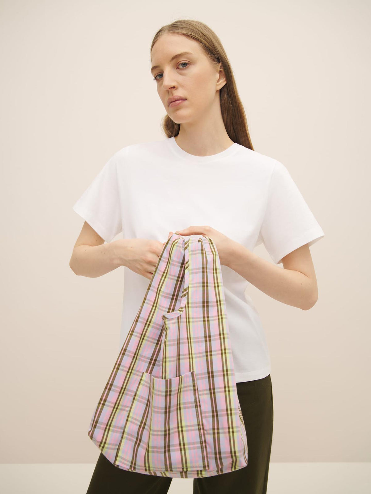 Woman holding a Kowtow Mini Market Bag in Pink Tartan and wearing a white t-shirt.