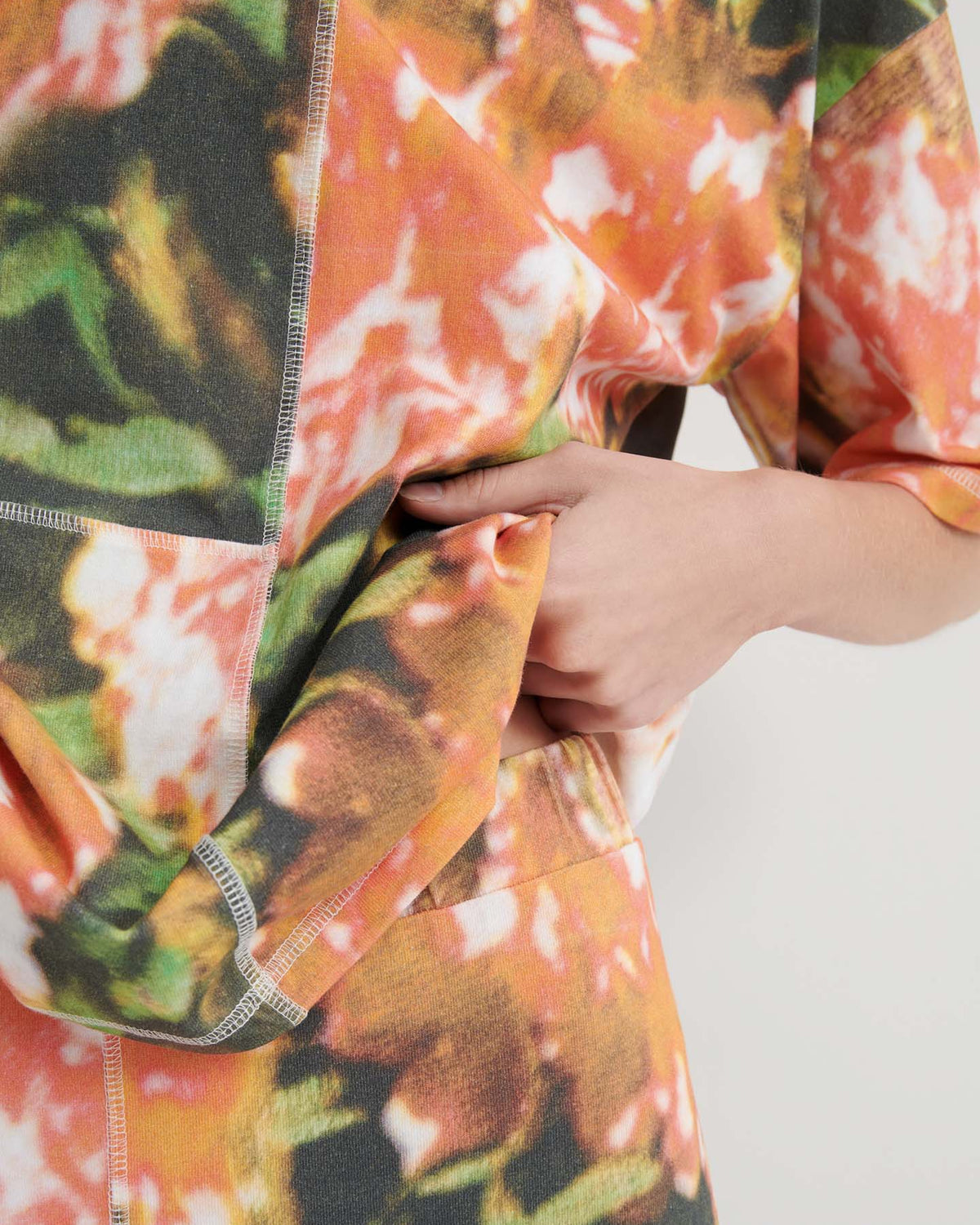 A person wearing the Montage Tee – Flower Book, featuring a colorful abstract pattern and relaxed fit, holds part of their shirt with one hand, partially revealing the side of their torso.