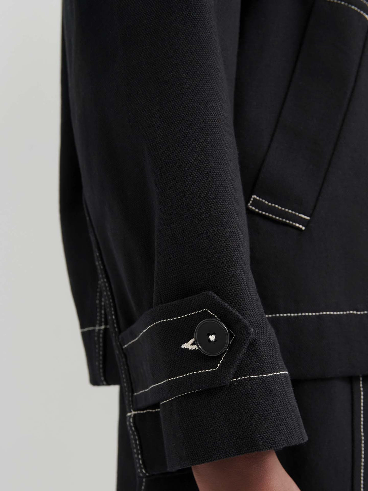 Close-up of an arm wearing the oversized Mural Jacket – Black, designed with drop shoulder sleeves, white contrast stitching, and a buttoned strap at the cuff.