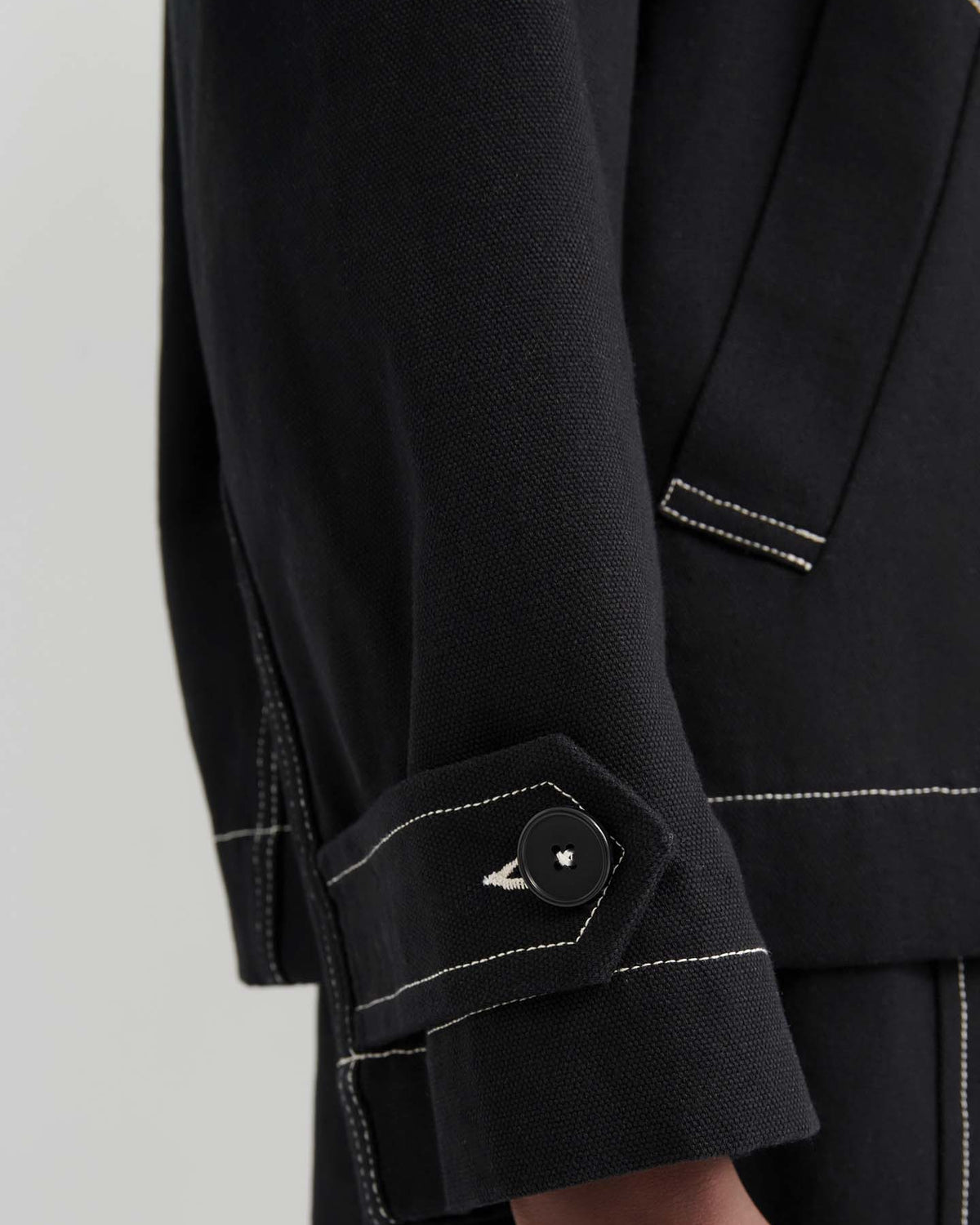 Close-up of an arm wearing the oversized Mural Jacket – Black, designed with drop shoulder sleeves, white contrast stitching, and a buttoned strap at the cuff.