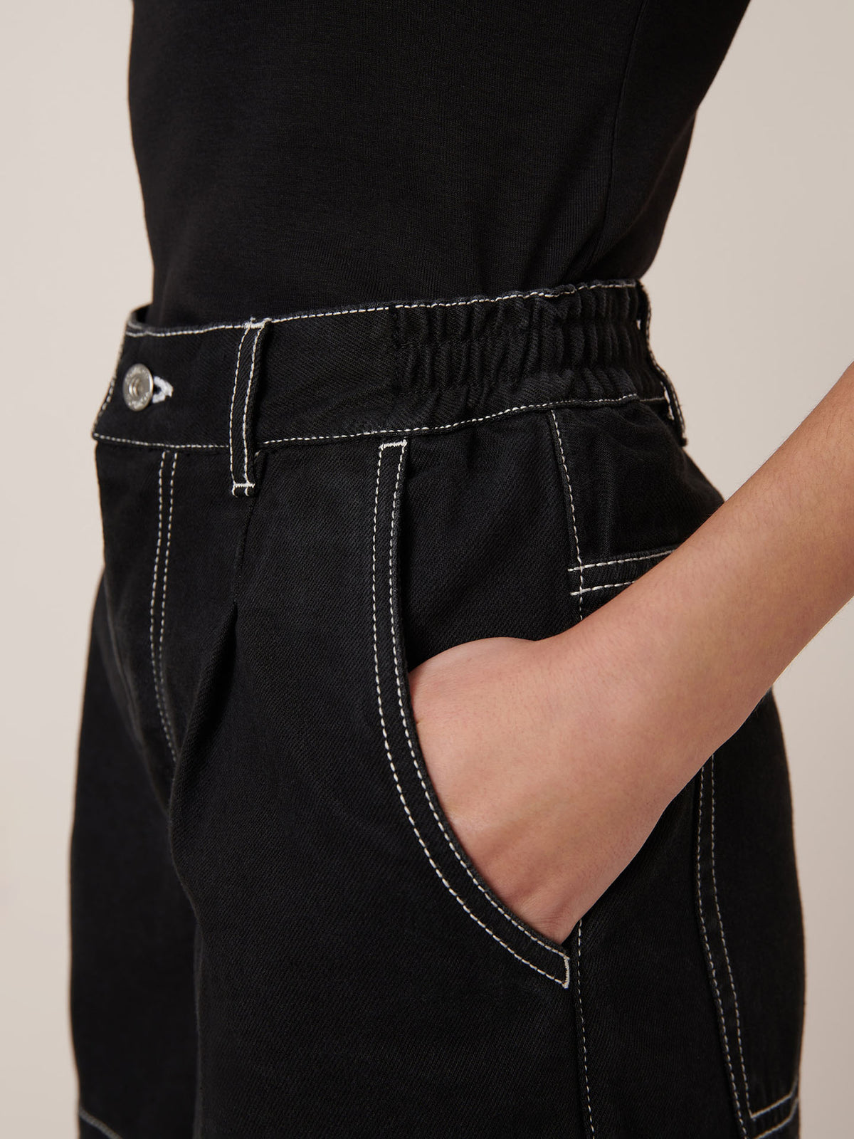 A person wears Kowtow&#39;s Outline Shorts in black with white contrast stitching, paired with a black top and their hand in the shorts pocket.