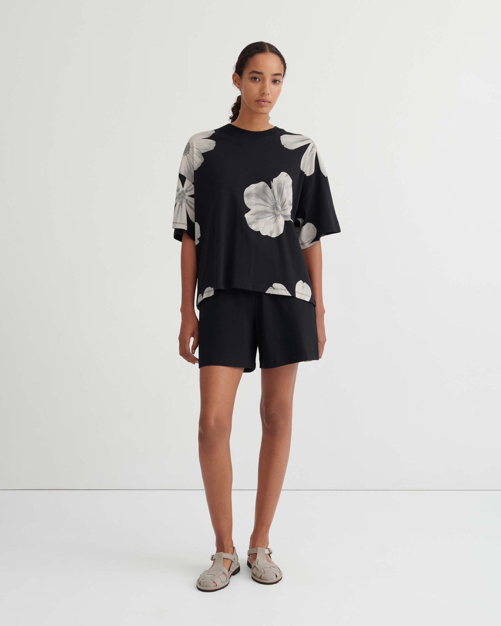 A person wears a black short-sleeved top featuring a white floral print and matching black shorts.