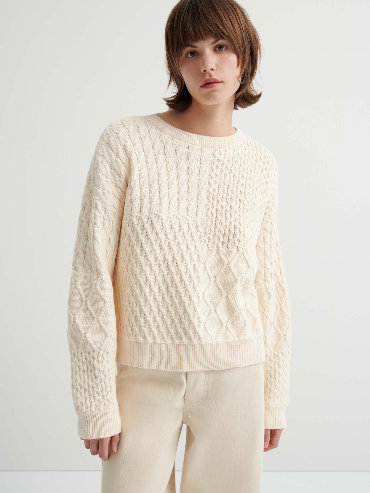 A person wears the Patchwork Jumper – Chalk, a cream-colored, textured knit with a boxy fit, paired with matching light beige pants against a plain light background.