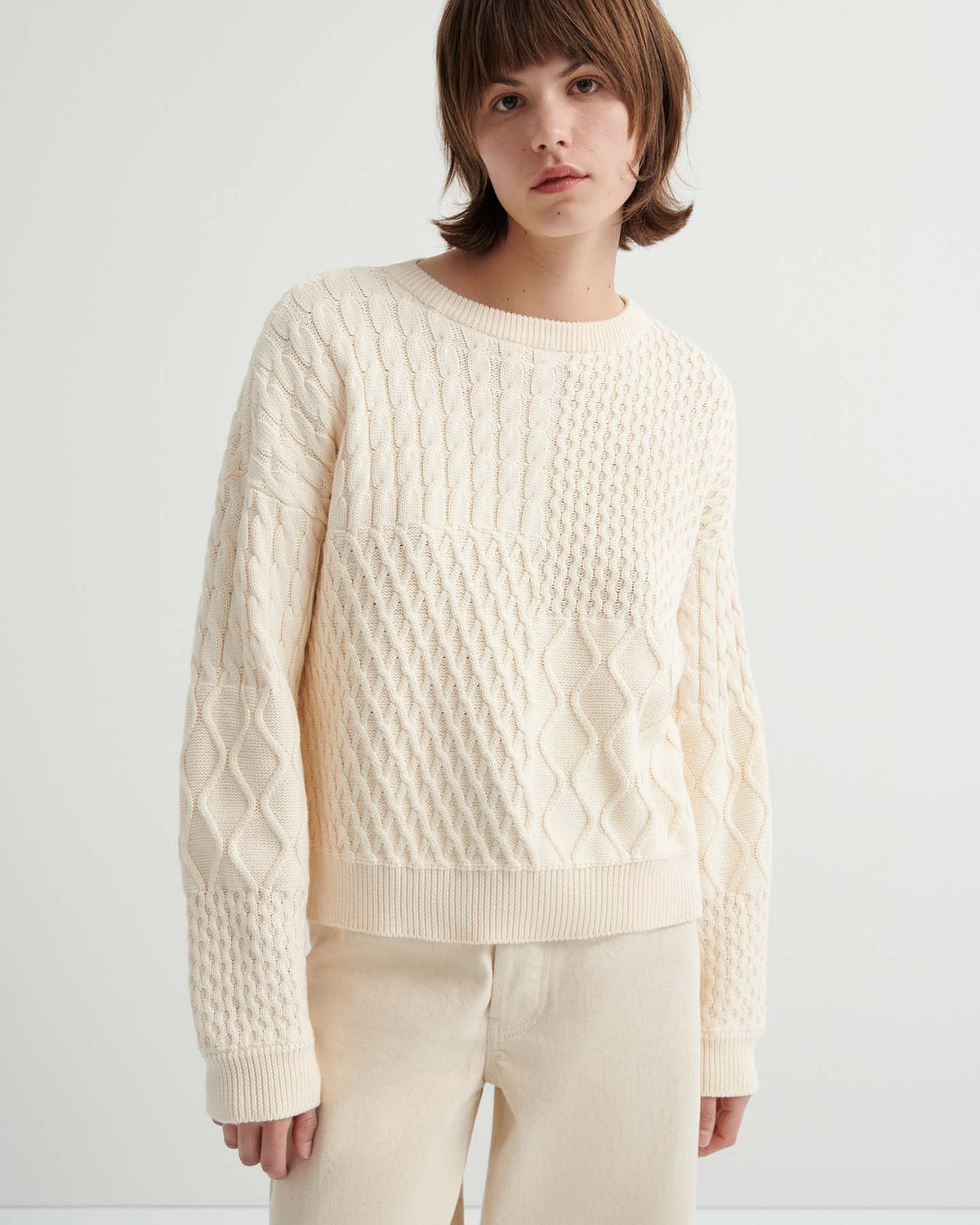 A person wears the Patchwork Jumper – Chalk, a cream-colored, textured knit with a boxy fit, paired with matching light beige pants against a plain light background.