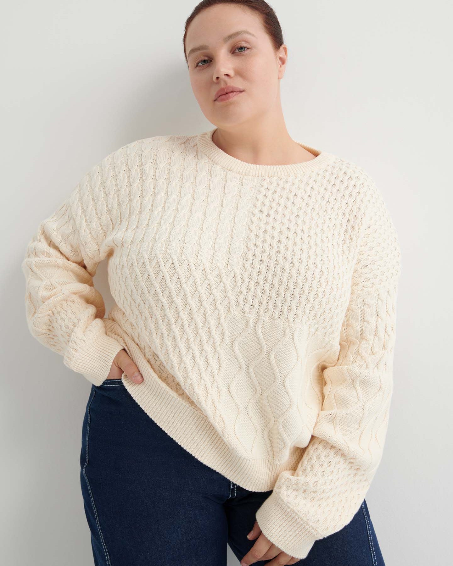 A person wears the Patchwork Jumper – Chalk, a cream-colored textured knit with a boxy silhouette, paired with dark blue jeans, standing against a plain white background.