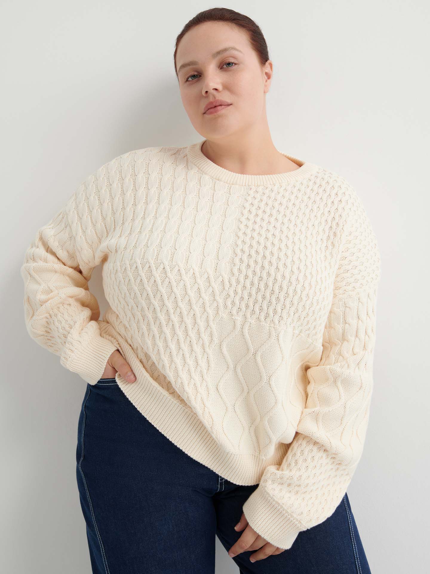 A person wears the Patchwork Jumper – Chalk, a cream-colored textured knit with a boxy silhouette, paired with dark blue jeans, standing against a plain white background.