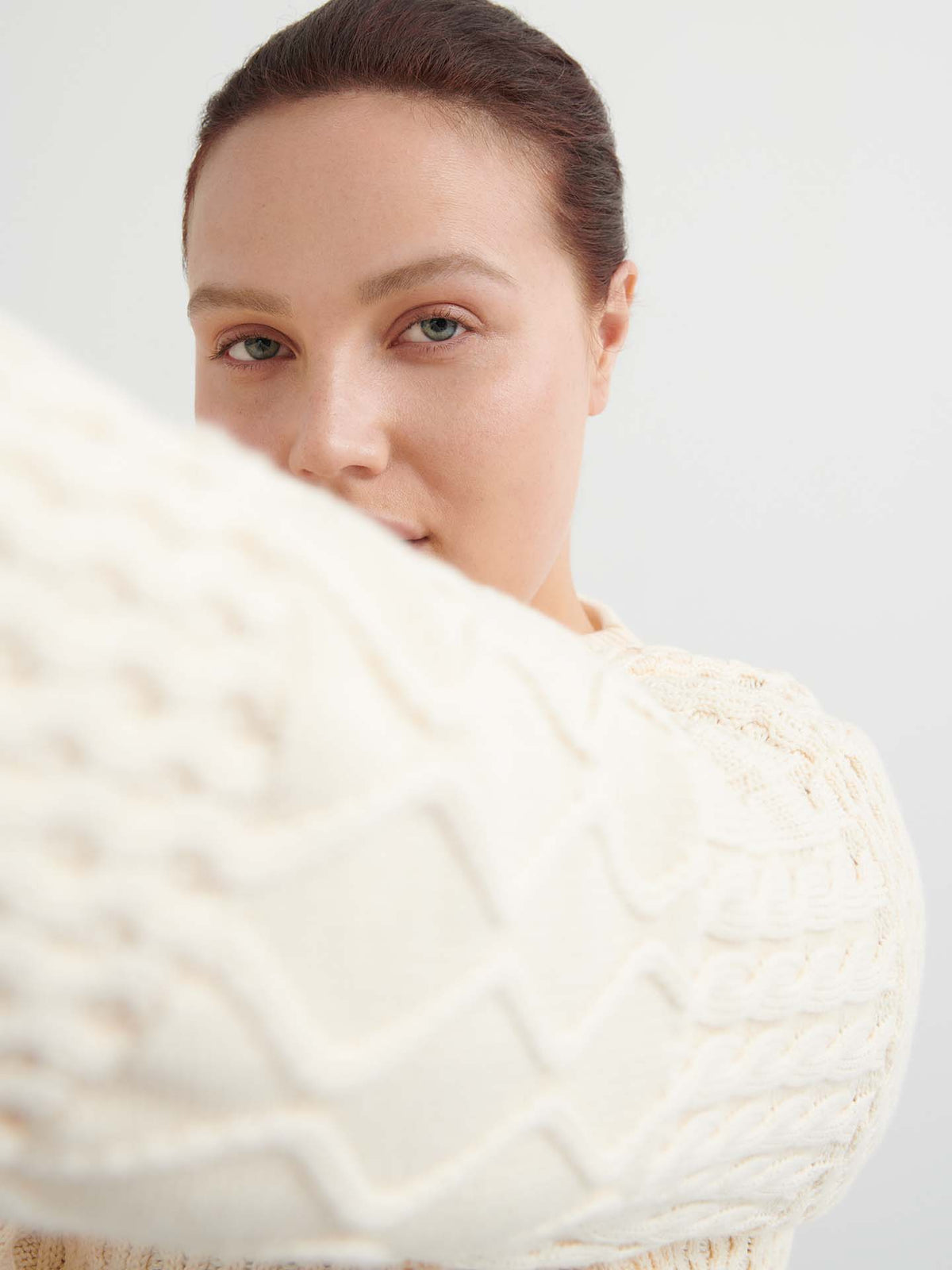 A person with fair skin and brown hair wears the Patchwork Jumper – Chalk in an oversized fit, holding one arm toward the camera and partially obscuring their face.