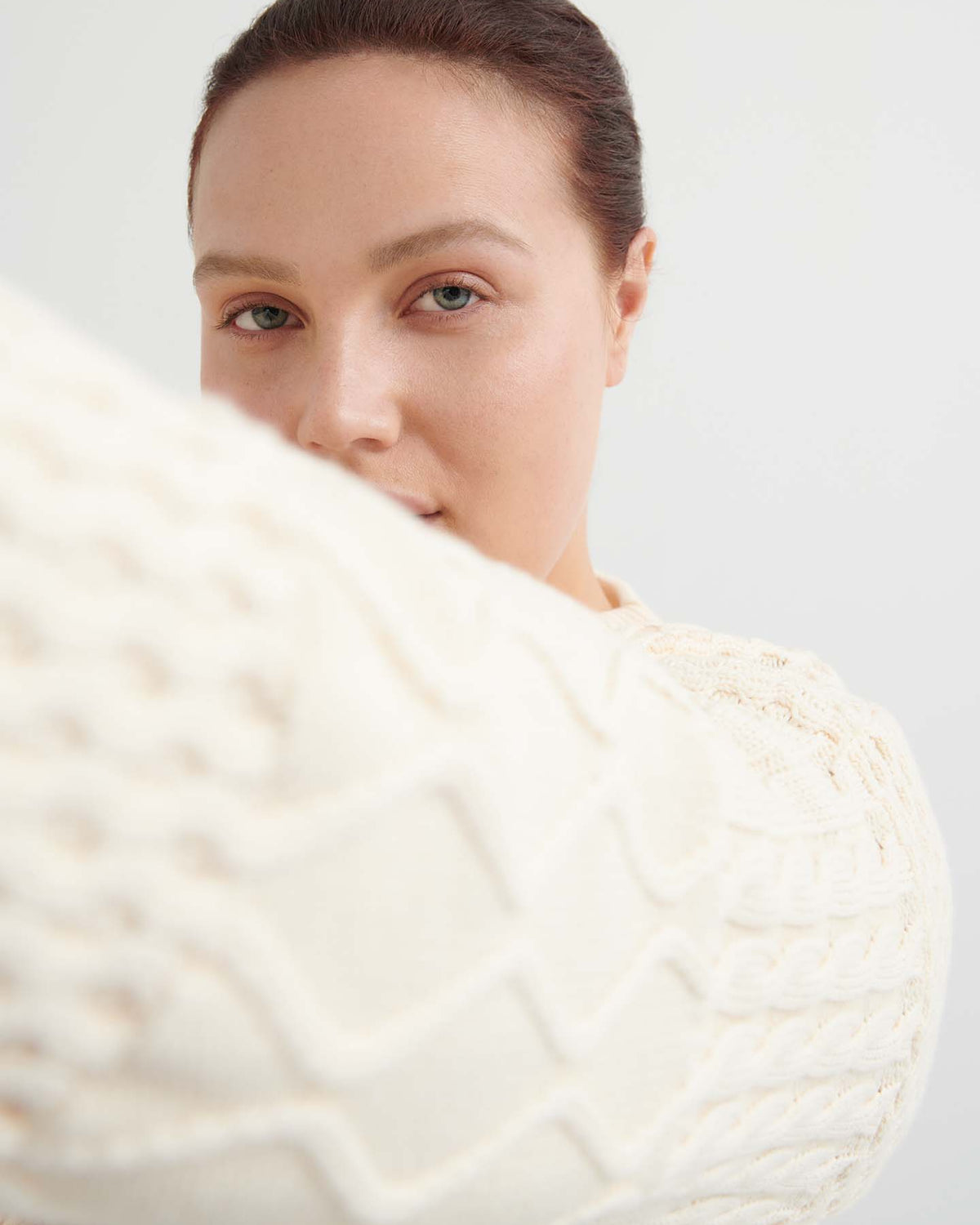 A person with fair skin and brown hair wears the Patchwork Jumper – Chalk in an oversized fit, holding one arm toward the camera and partially obscuring their face.