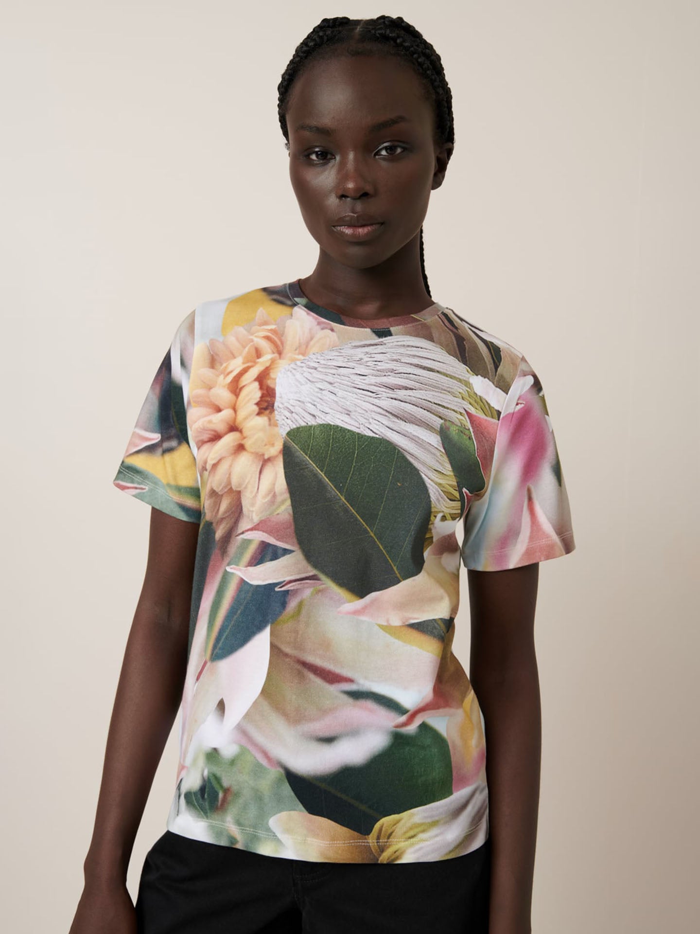 A person models the Kowtow Protea Tee, an oversized T-shirt featuring a bold floral print, standing against a plain, light background.