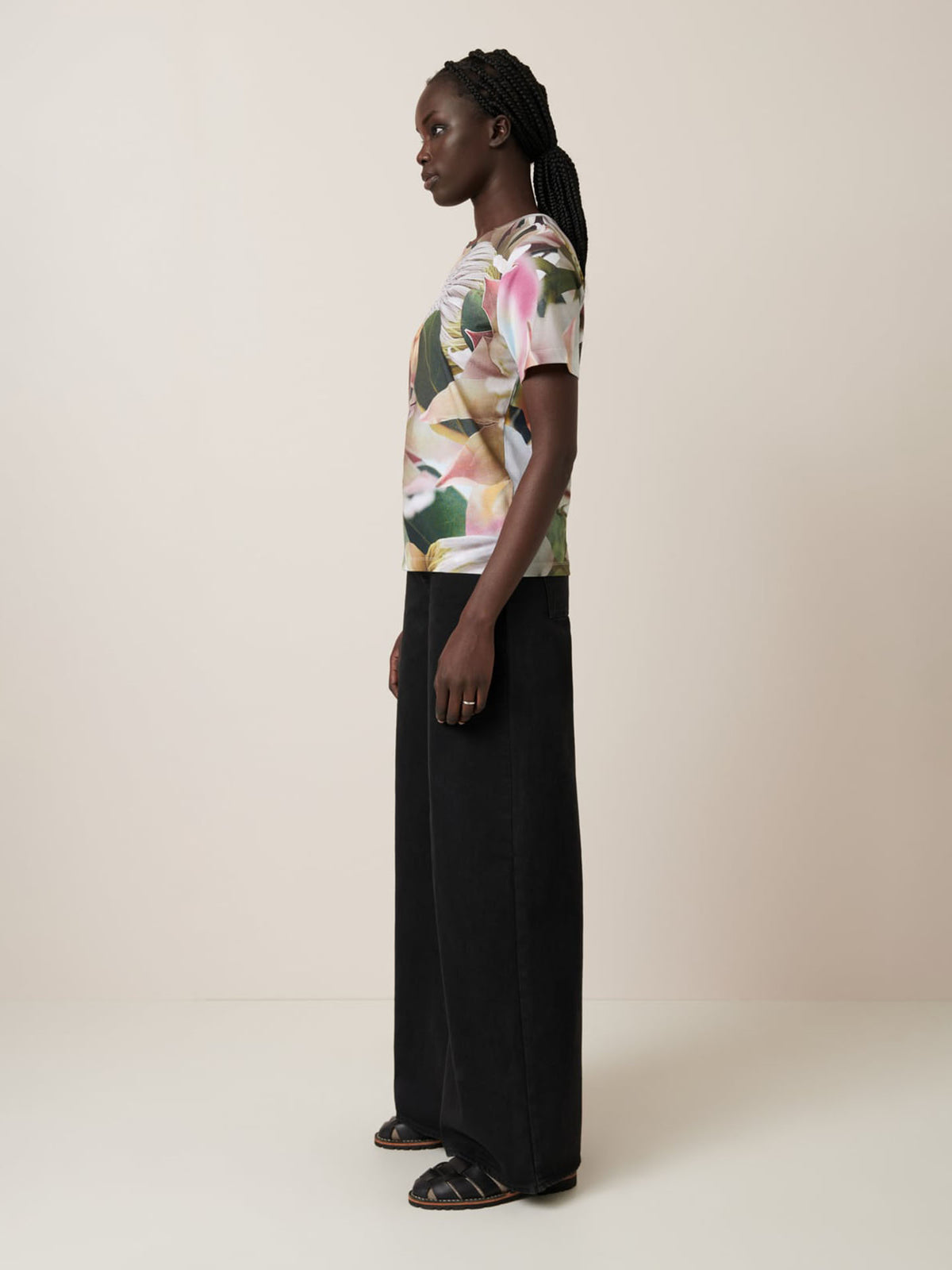 Woman standing in profile against a plain background, wearing the Kowtow Protea Tee—an oversized fit floral short-sleeve top—paired with wide-leg black trousers and black sandals. See size guide for measurements.