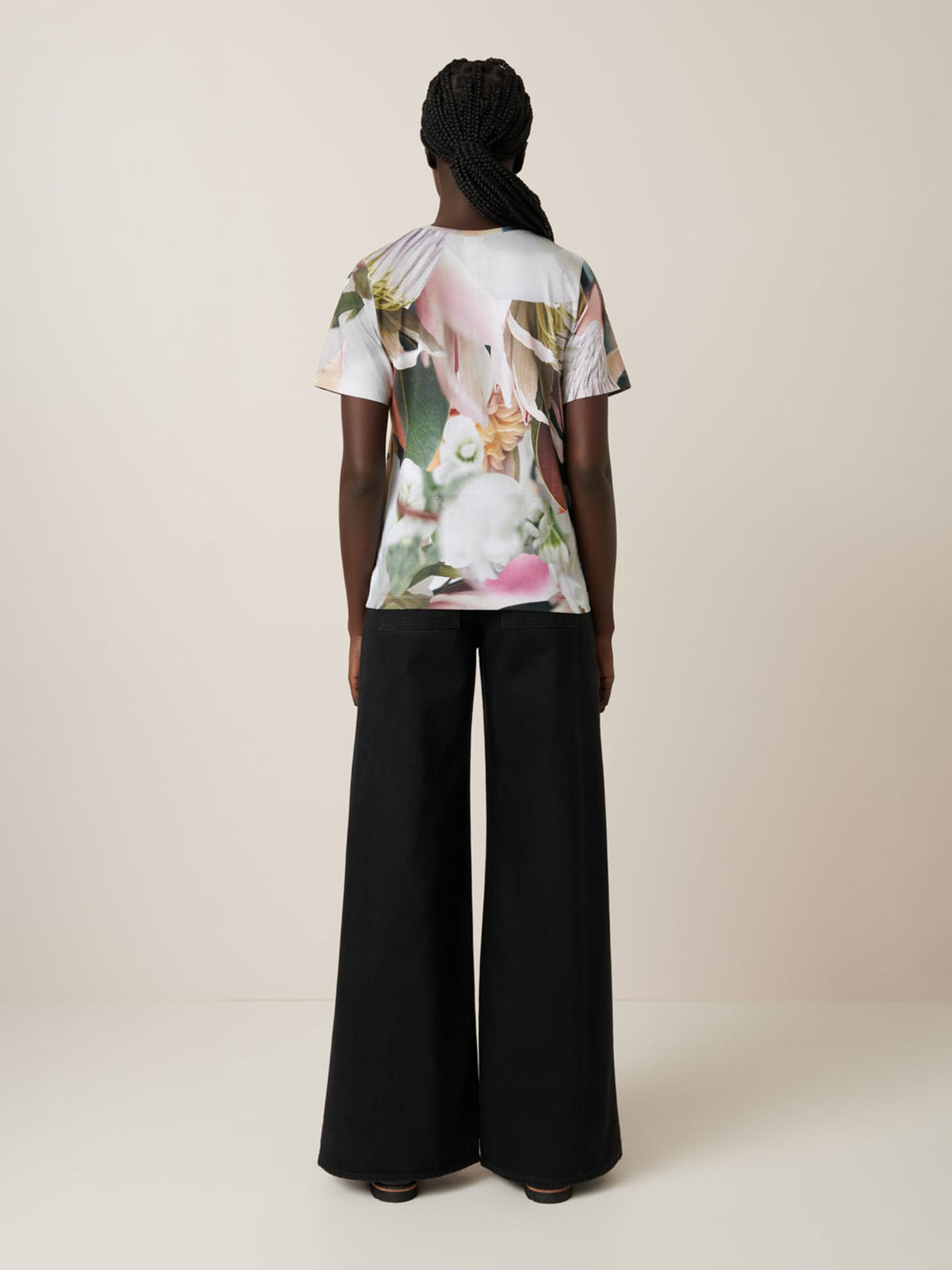 Person stands facing away, wearing the Kowtow Protea Tee—an oversized floral t-shirt—paired with wide-leg black pants against a plain light background.