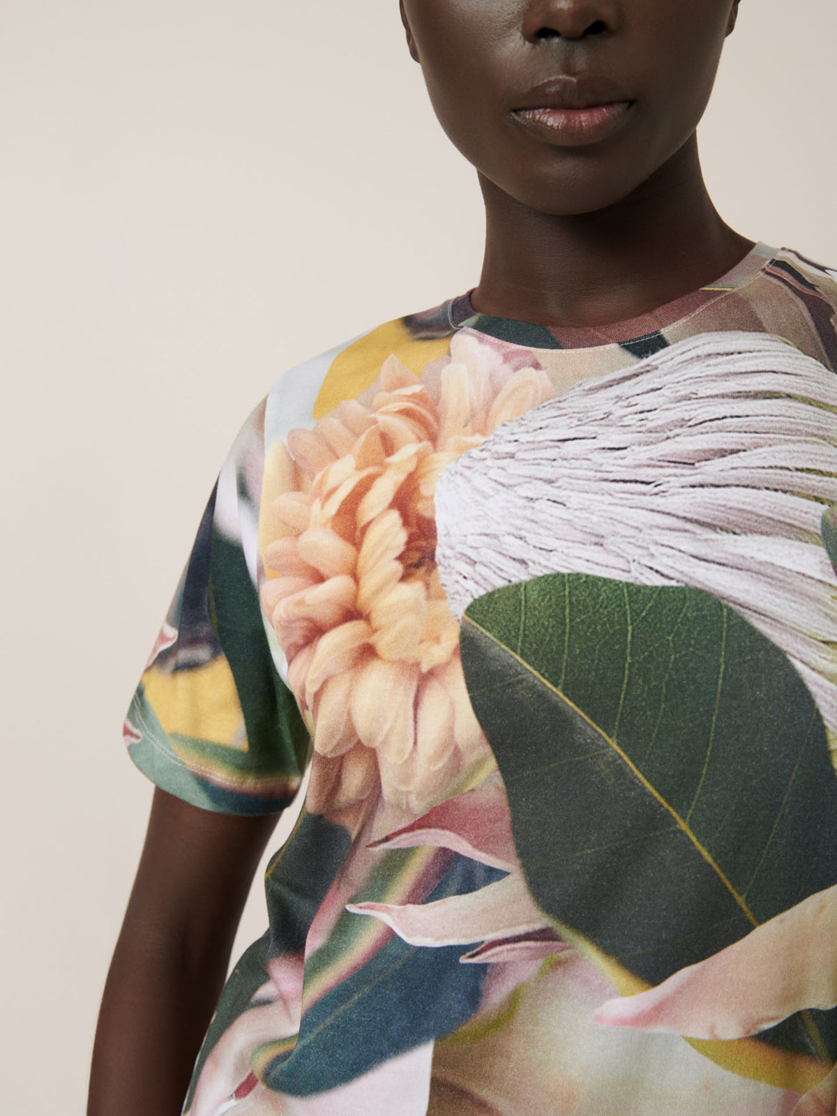 A person wears the Kowtow Protea Tee, an oversized t-shirt with a bold floral and leaf print. For a comfy fit, see our size guide for measurements.