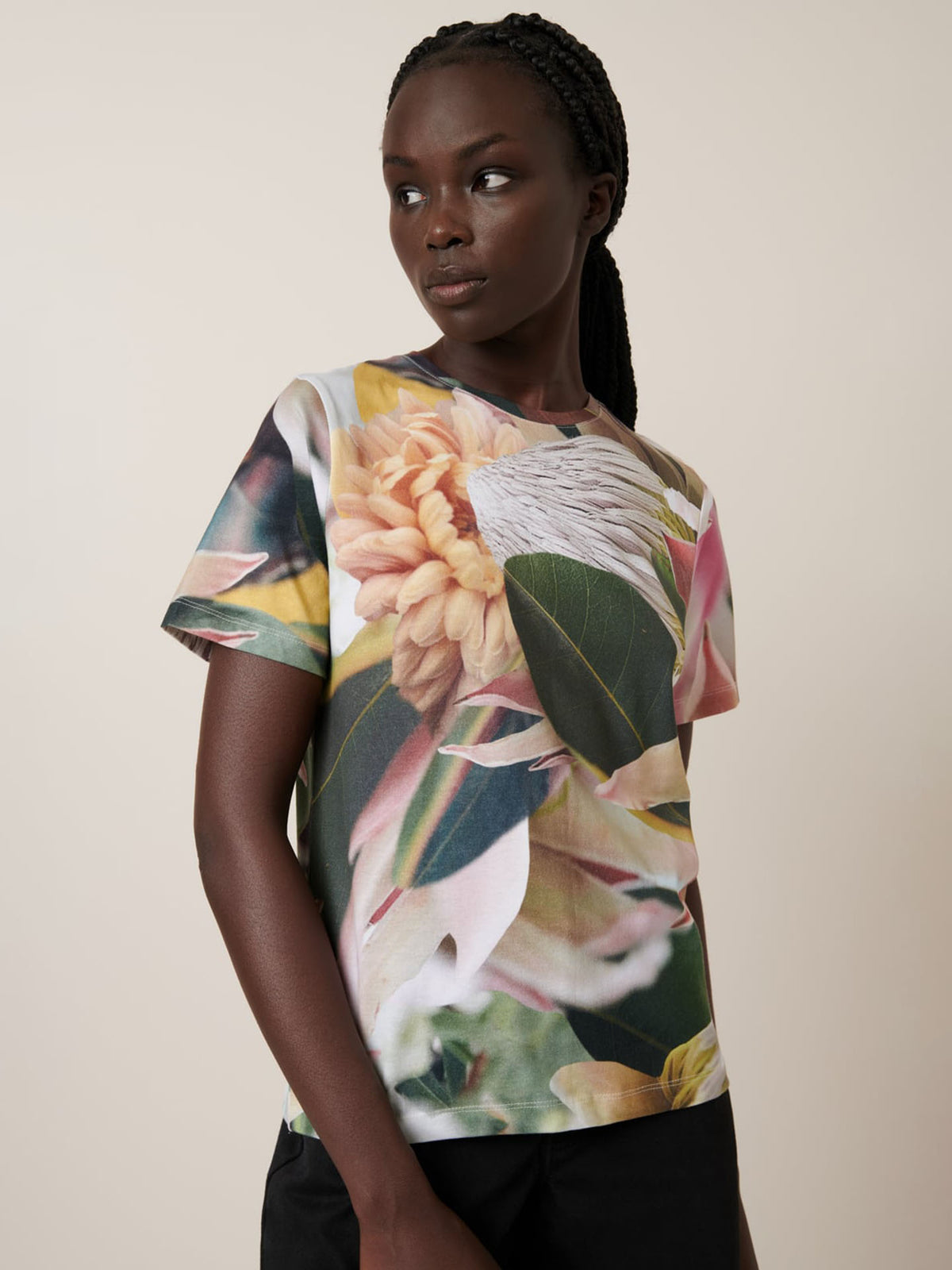 A person wears the Kowtow Protea Tee—an oversized short-sleeve t-shirt featuring a large floral print—while standing against a plain light background.