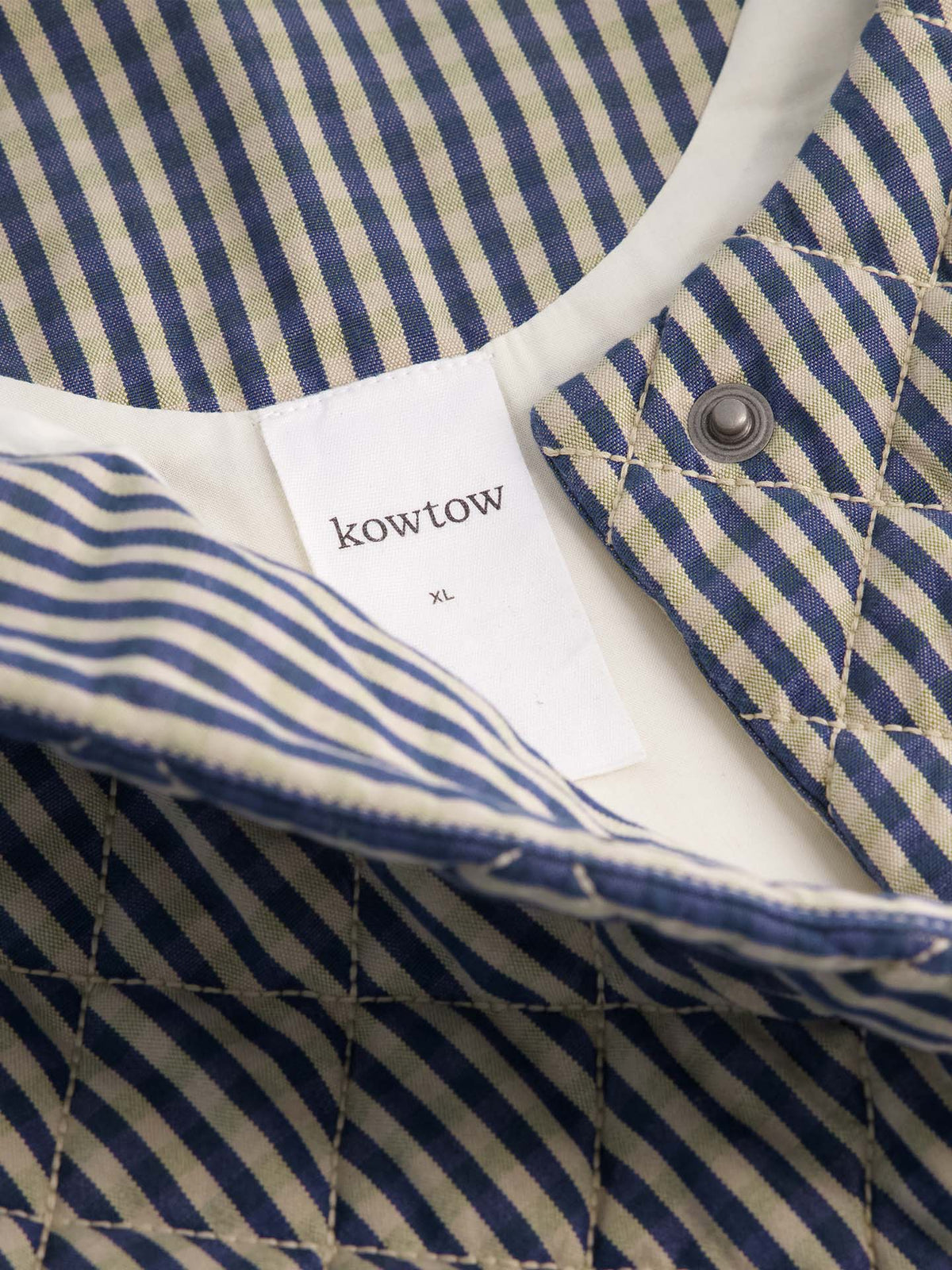 Close-up of the Quilter Vest – Landscape check, featuring striped quilting, a visible "kowtow XL" label, and metal snap button—perfect for layering with its relaxed fit.
