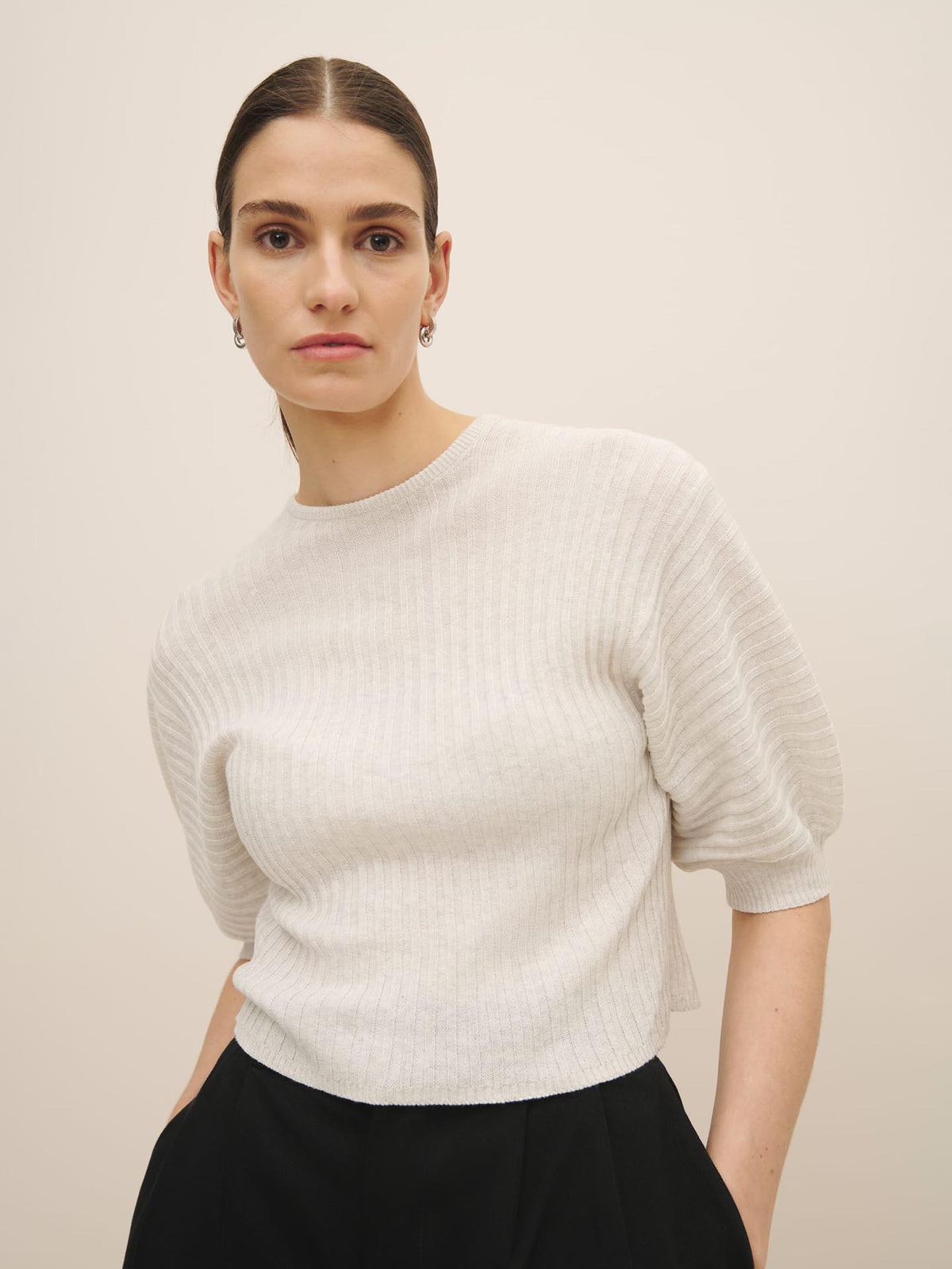 Woman in a Quinn Top - Light Marle by Kowtow and black skirt, both ethically made, posing against a neutral background.
