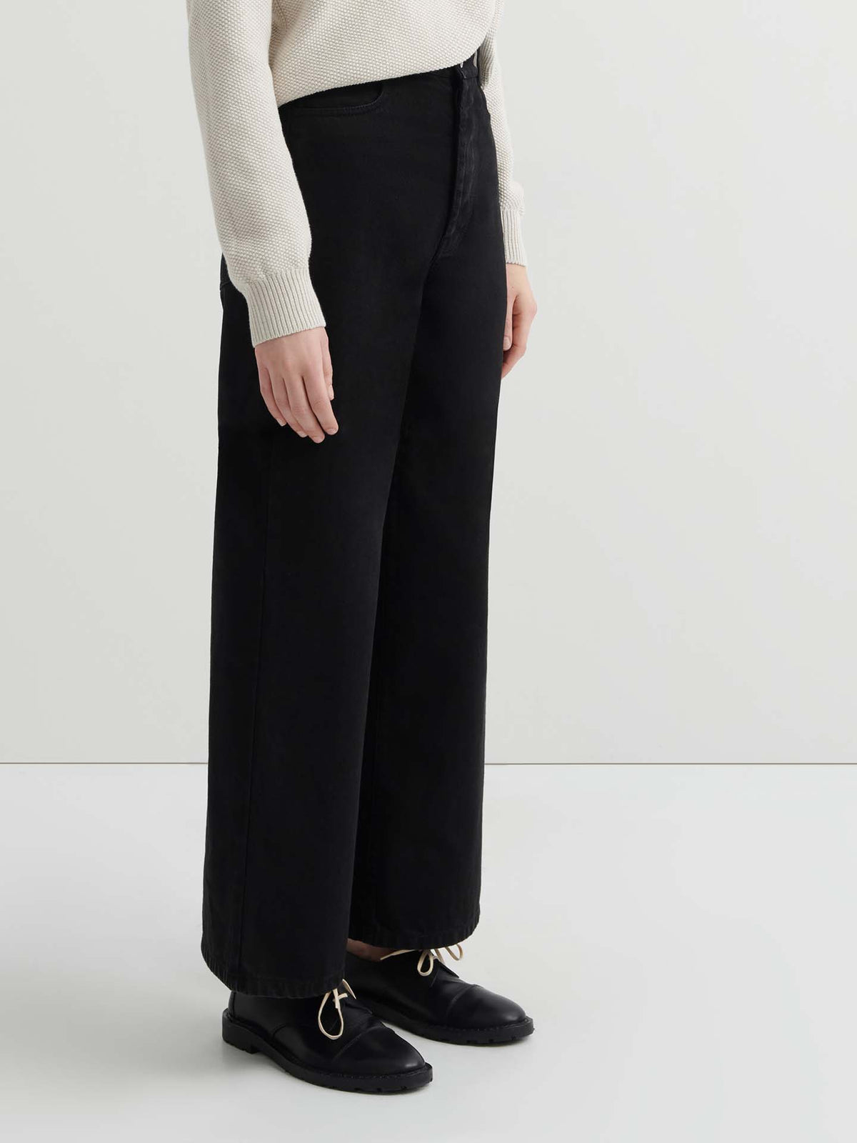 Person wearing a cream knit sweater, Sailor Jeans – Black Denim (relaxed fit, wide-leg), and black shoes, standing against a plain white background.