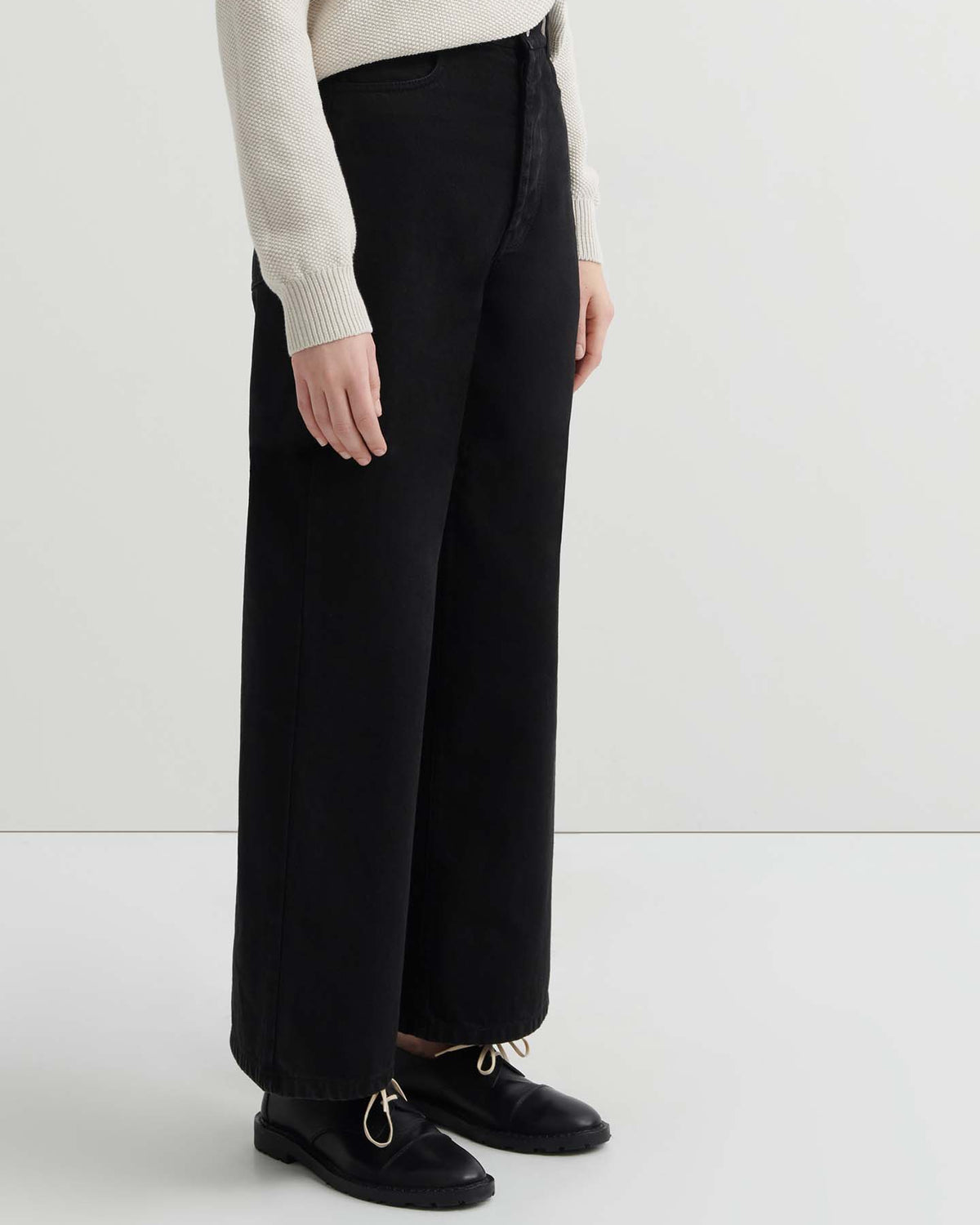 Person wearing a cream knit sweater, Sailor Jeans – Black Denim (relaxed fit, wide-leg), and black shoes, standing against a plain white background.