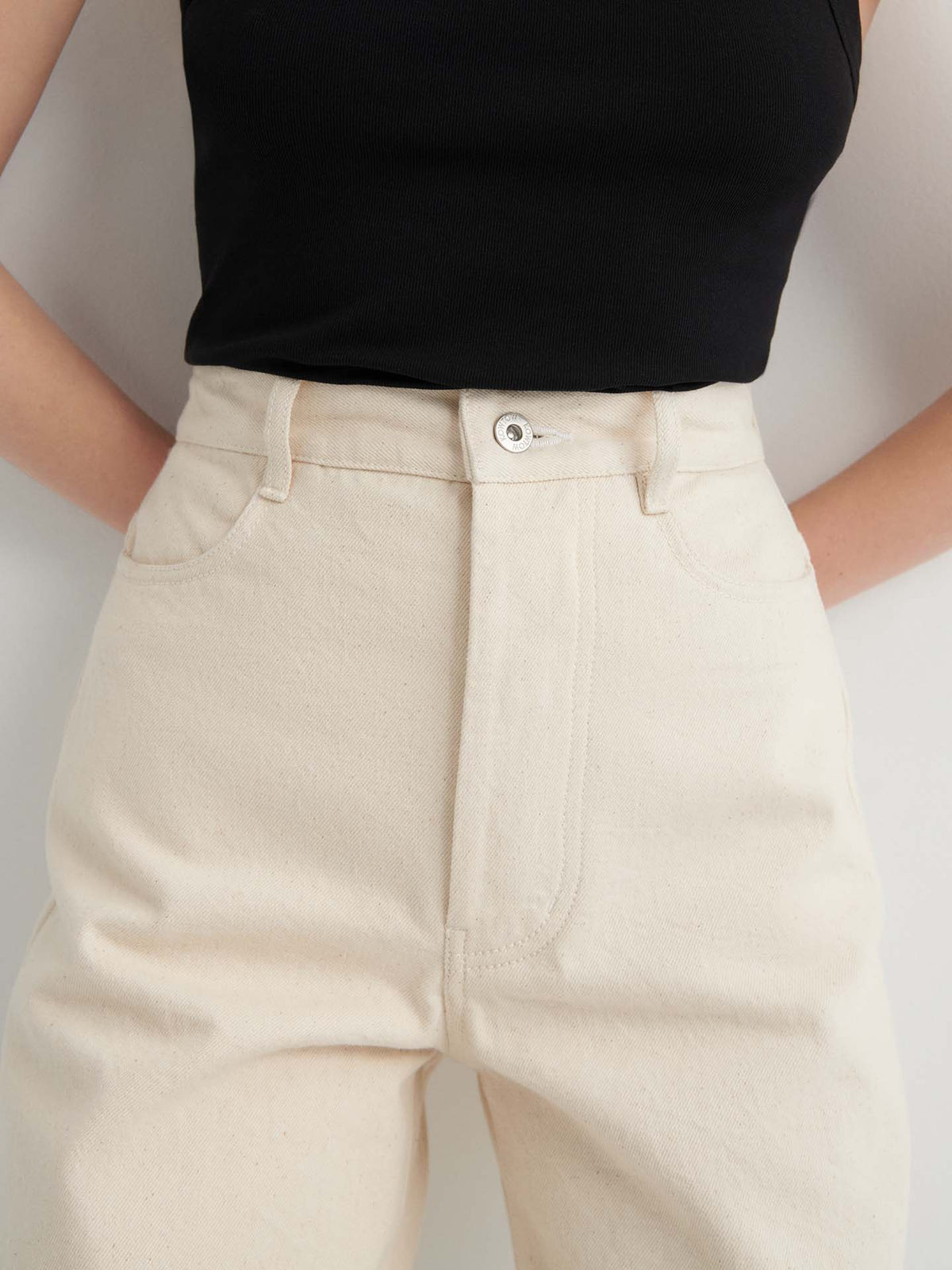 Wearing Sailor Jeans – Ecru Denim, high-waisted with a relaxed fit, paired with a black sleeveless top against a plain background.