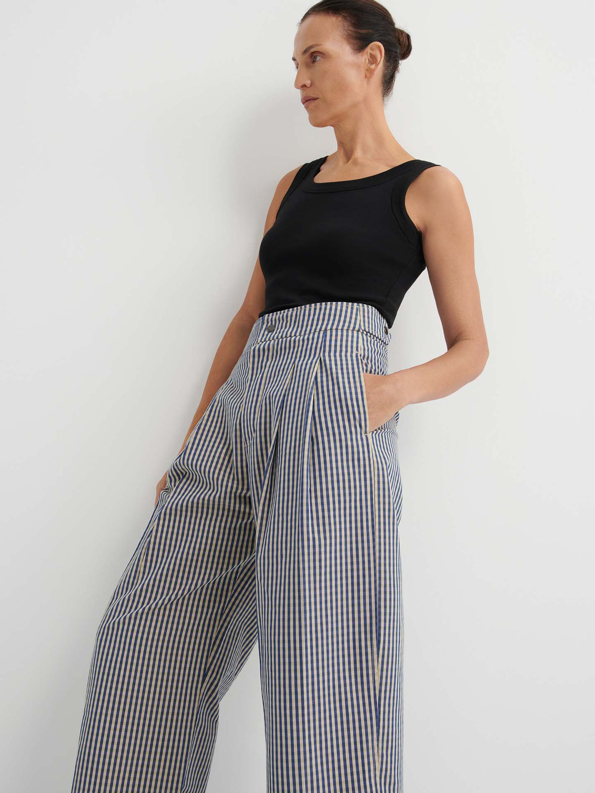 A woman stands against a white background with her hands in her pockets, wearing a black sleeveless top and high-waisted, wide-leg Sculpt Pant – Landscape Check featuring a fixed waistband and relaxed fit.