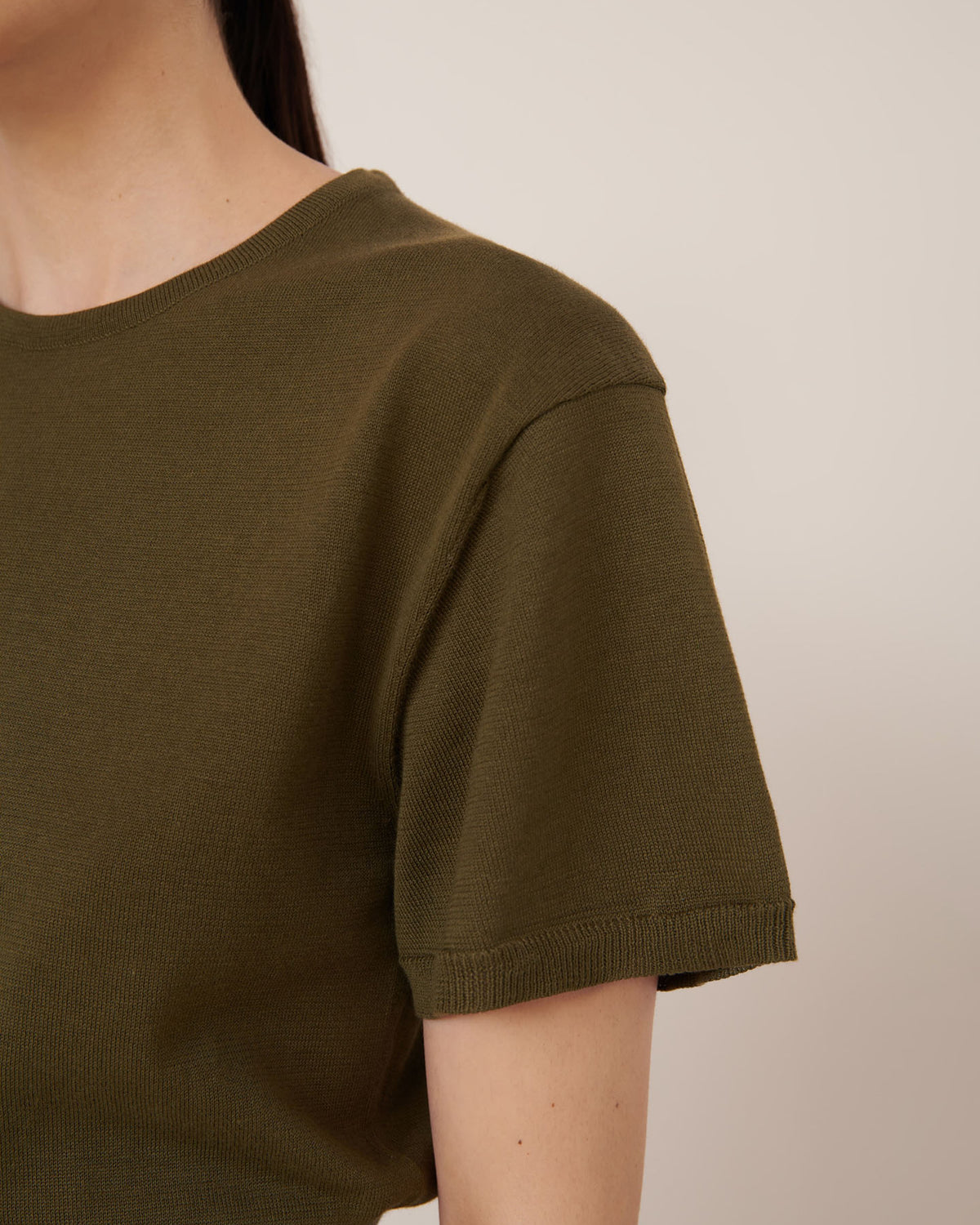 A person wearing the Kowtow Silhouette Top – Ivy, an olive green standard-fit short-sleeve knit, is photographed from the shoulder up against a plain background.