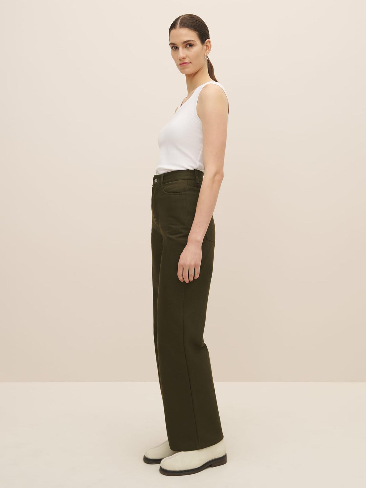 The model is wearing a white tank top and green trousers made with organic cotton by Kowtow.
