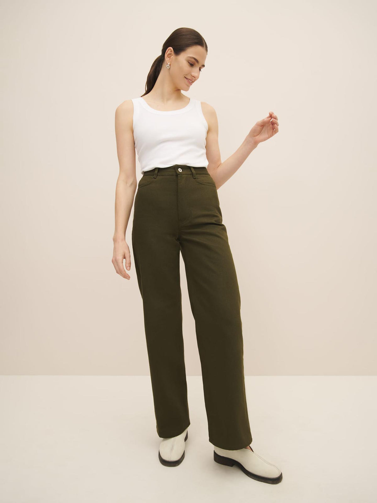 A woman wearing a white tank top and green wide leg pants made of organic cotton.