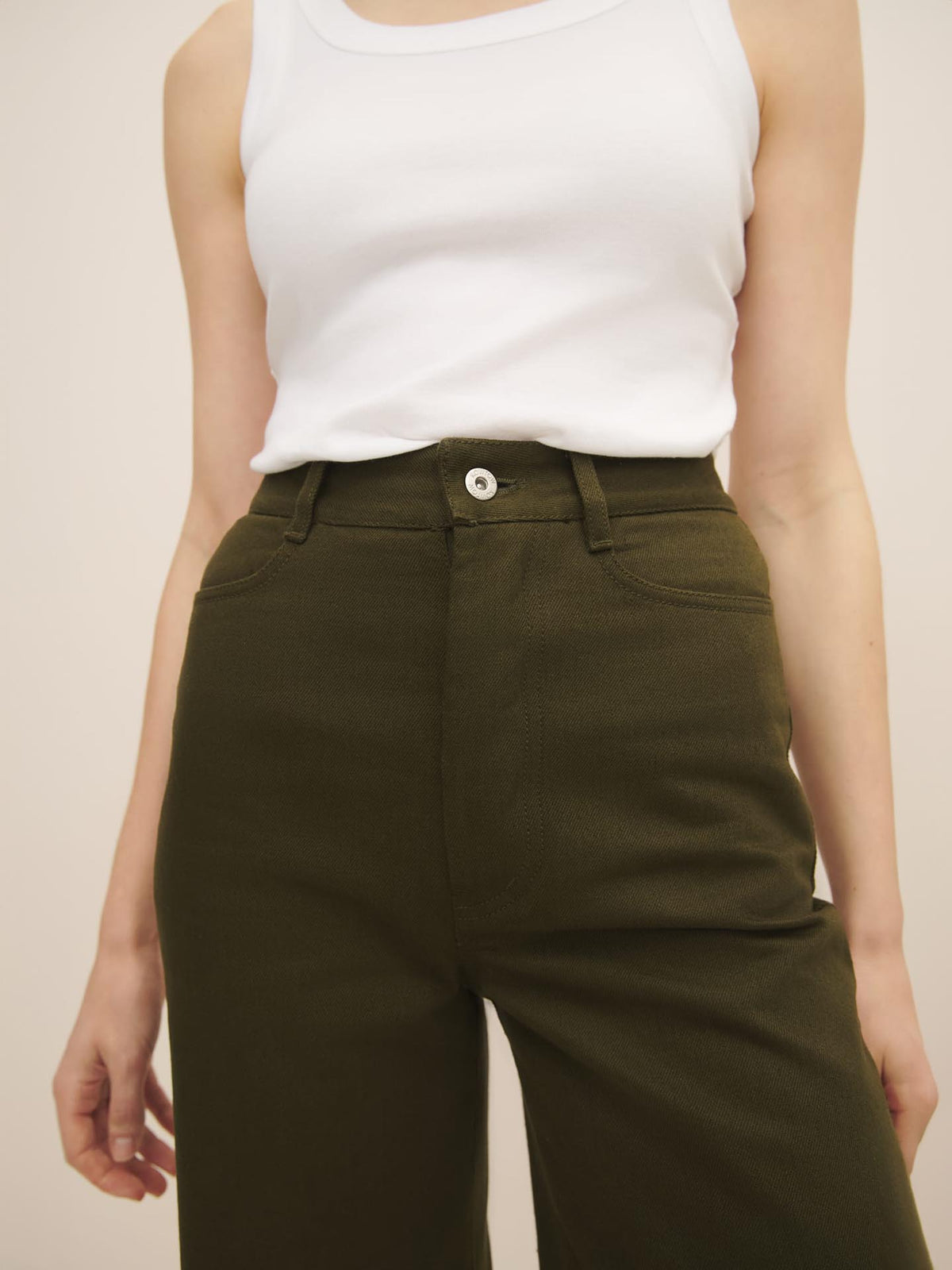 A woman wearing a white tank top made of organic cotton and Kowtow straight leg jeans – khaki denim.
