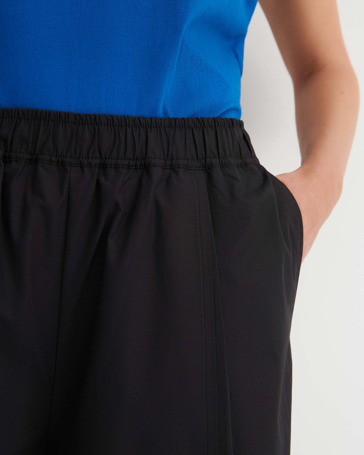 Person wearing a blue top and black elastic-waist pants with a hand in the pocket, shown from shoulder to mid-thigh against a plain background.
