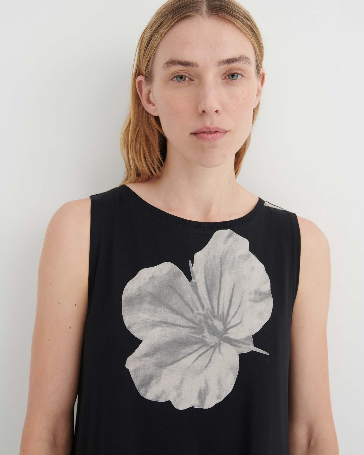 A person wearing a sleeveless black top featuring a large, gray floral print.