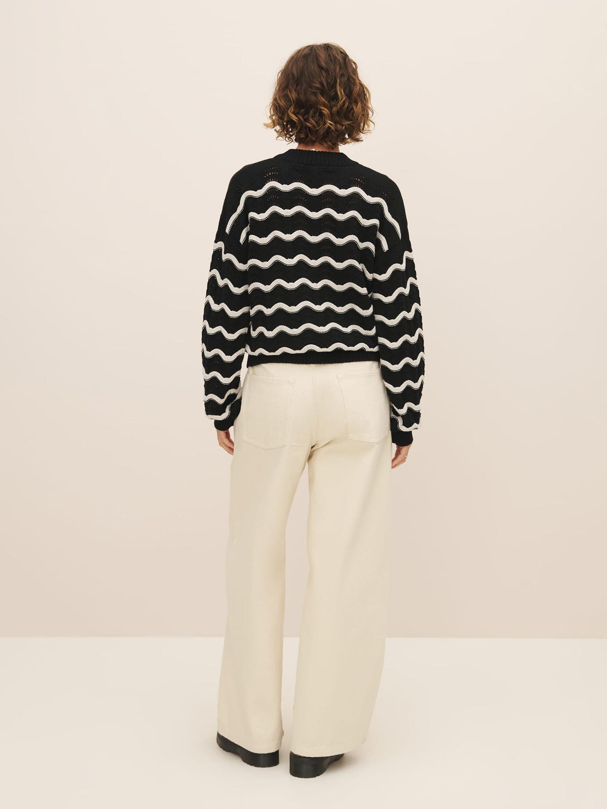 Person standing with their back to the camera wearing a Kowtow Tide Jumper made from Fairtrade organic cotton and beige pants.