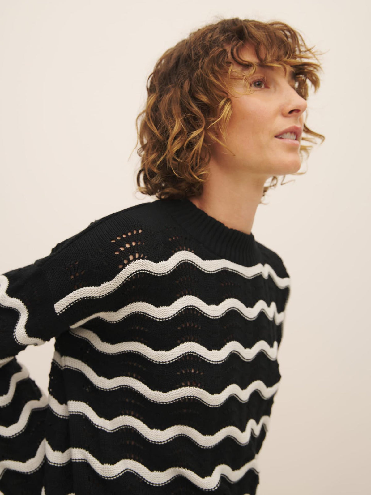 Woman with curly hair wearing a striped Tide Jumper made from Fairtrade organic cotton by Kowtow, looking to the side.