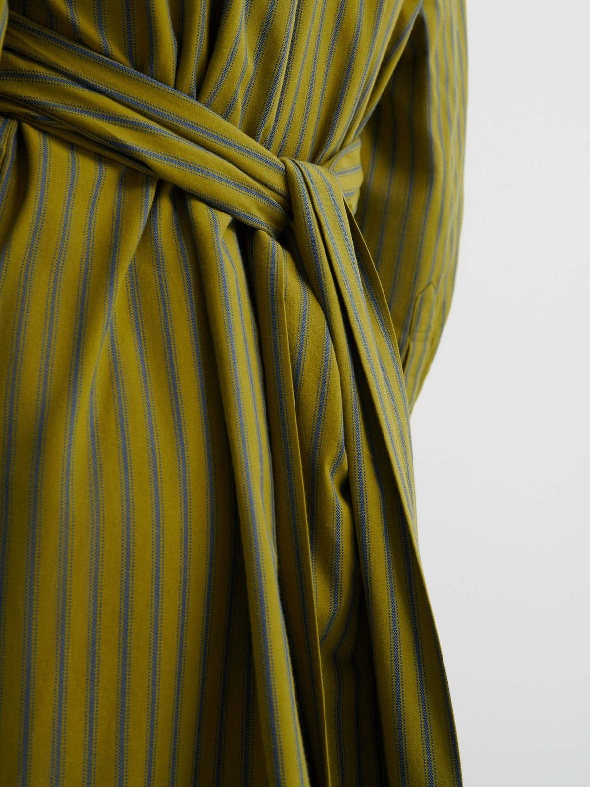 Close-up of the Twist Dress – Artisan Stripe in yellow-green and blue stripes, tied at the waist with a matching belt to highlight its relaxed fit against a plain light background.