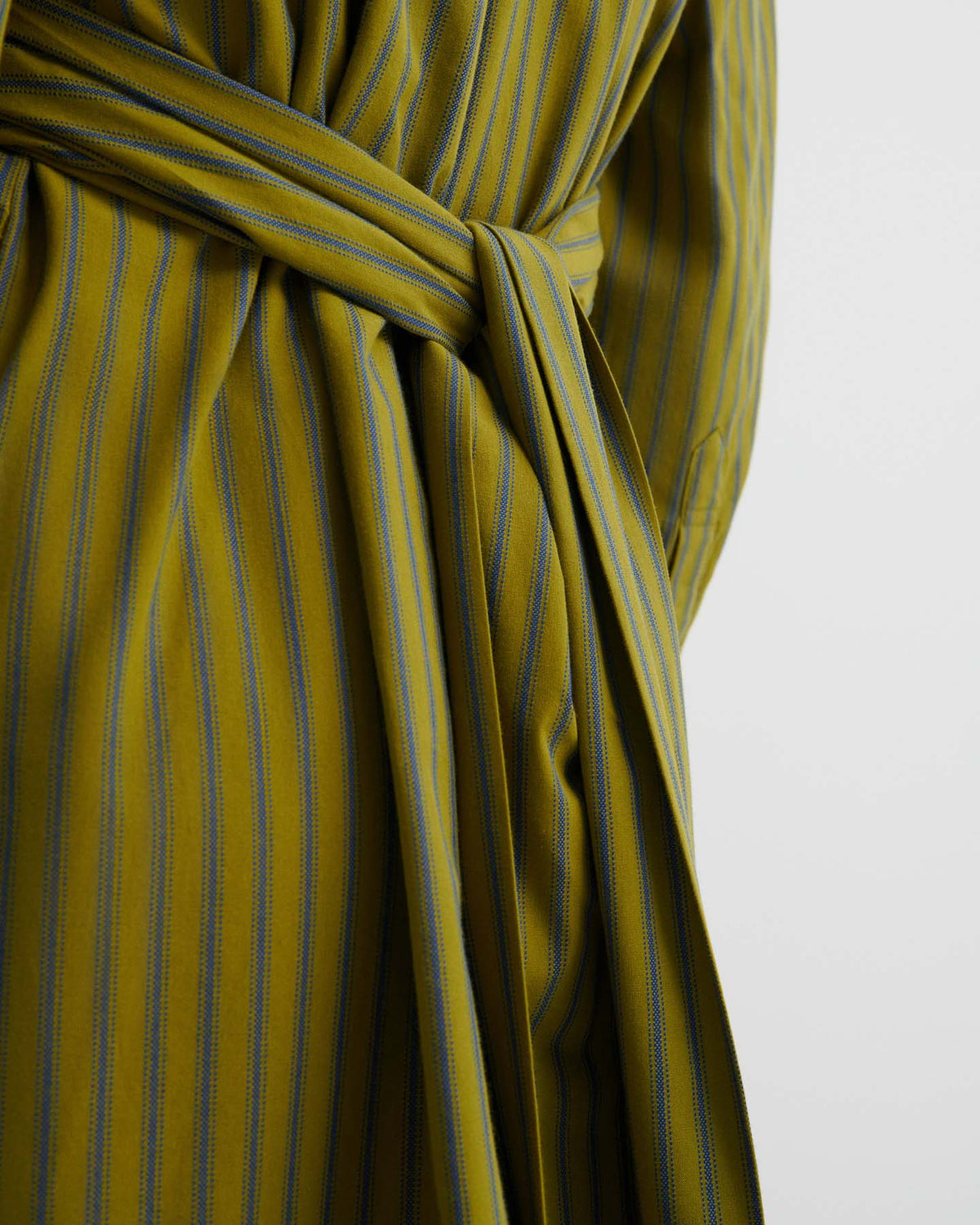 Close-up of the Twist Dress – Artisan Stripe in yellow-green and blue stripes, tied at the waist with a matching belt to highlight its relaxed fit against a plain light background.