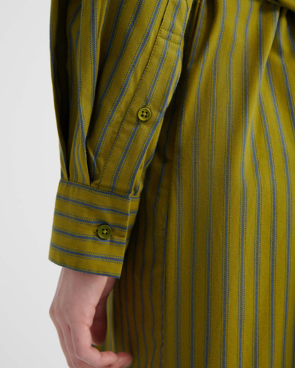A close-up of a person’s arm wearing the Twist Dress – Artisan Stripe, featuring green and blue stripes with a relaxed fit, highlighting the buttoned cuff on the sleeve and part of their hand.