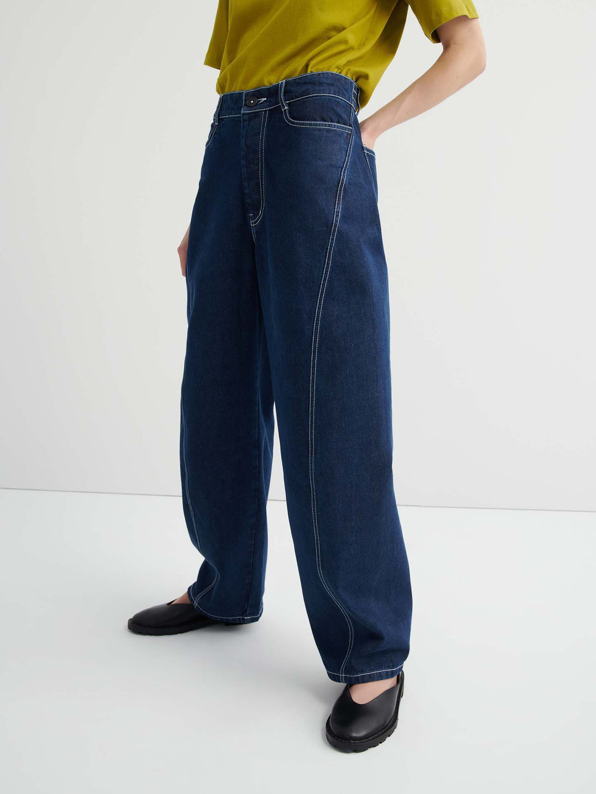 A person wearing Twist Jeans – Indigo Denim, a yellow-green short-sleeve top, and black shoes stands against a plain white background.