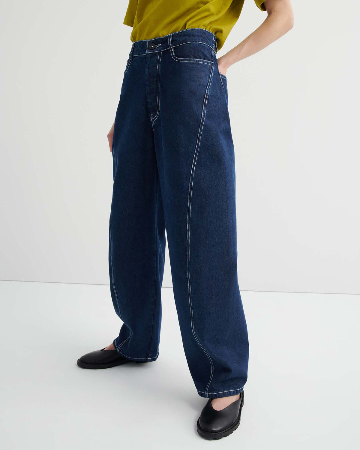 A person wearing Twist Jeans – Indigo Denim, a yellow-green short-sleeve top, and black shoes stands against a plain white background.
