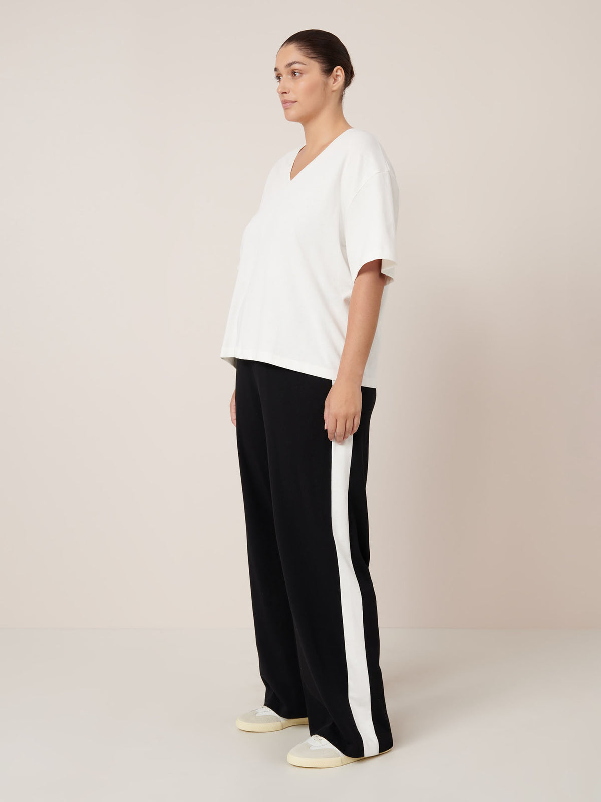 Wearing the Kowtow Unity Tee in Off White, paired with black wide-leg pants with a white side stripe and white sneakers, this person embodies easy style that flatters any Kowtow size against a simple background.