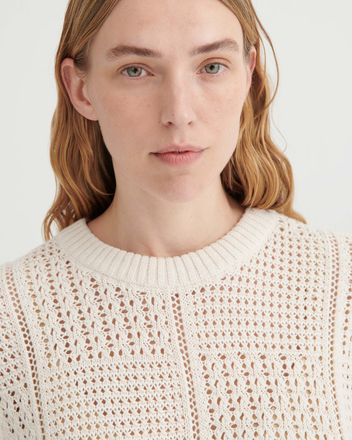 A woman wearing a cream-colored, open-knit sweater.