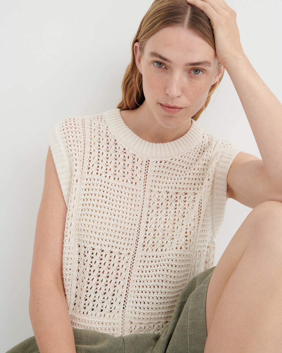 A woman wearing a cream-colored, sleeveless open-knit sweater top.