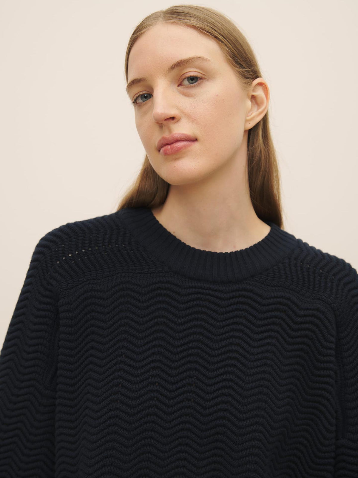 A woman with light brown hair wearing a Kowtow Zig Zag Crew – Indigo sweater, facing the camera with a neutral expression.