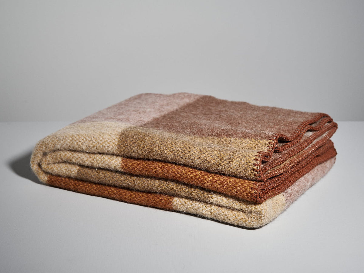 A neatly folded, multicolored Block Wool Throw – Rust by Klippan featuring shades of brown and beige lies on a plain white surface.