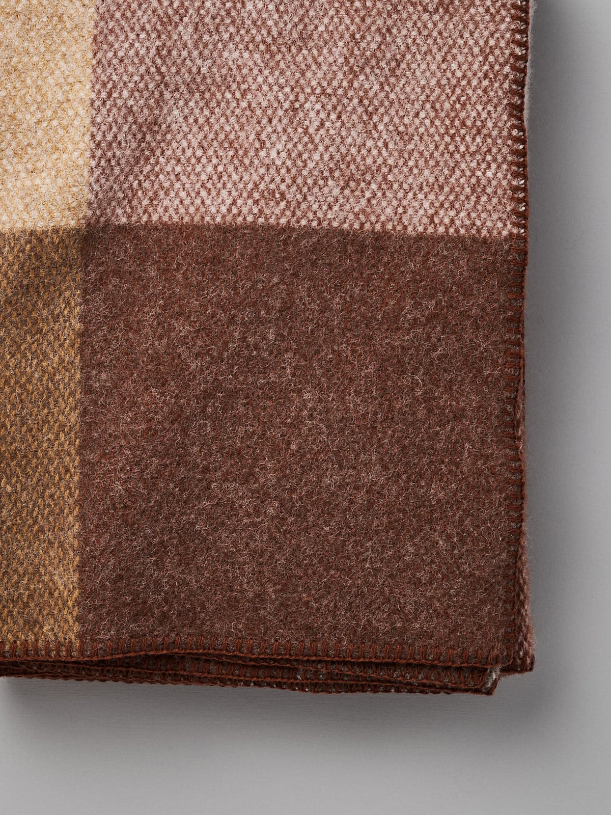 Folded Klippan Block Wool Throw – Rust with a checkered pattern in shades of brown, beige, and light pink, placed against a plain gray background.