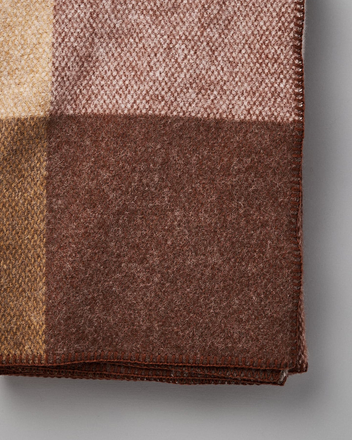 Folded Klippan Block Wool Throw – Rust with a checkered pattern in shades of brown, beige, and light pink, placed against a plain gray background.