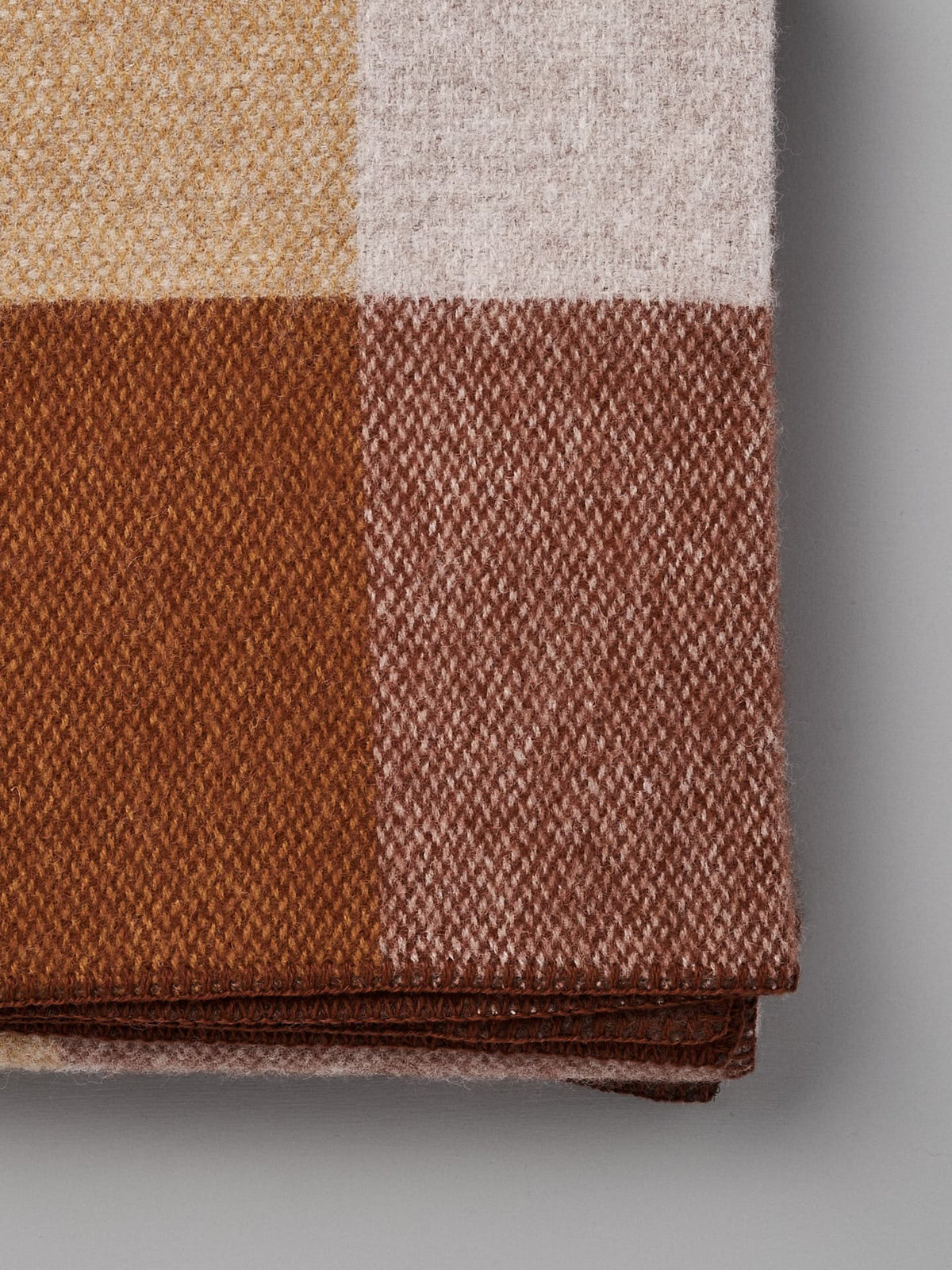 Close-up of a folded Klippan Block Wool Throw – Rust featuring a checkered pattern in shades of yellow, white, light brown, and dark brown.