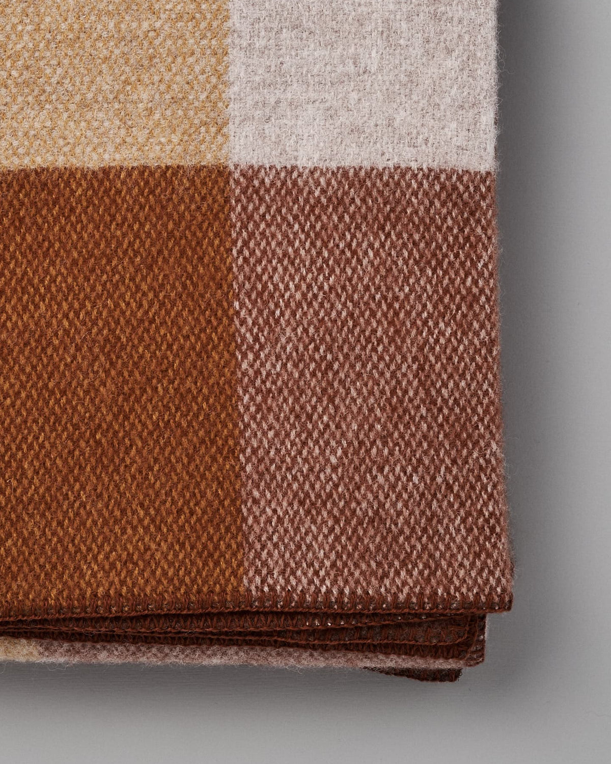 Close-up of a folded Klippan Block Wool Throw – Rust featuring a checkered pattern in shades of yellow, white, light brown, and dark brown.