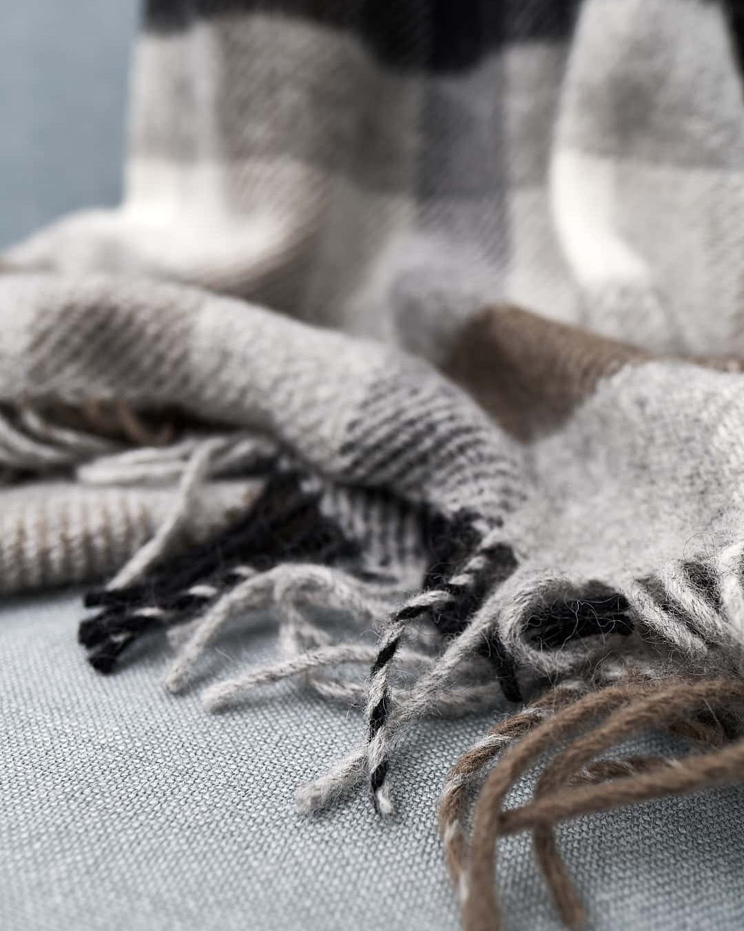 A Gotland Wool Throw – Multi Grey by Klippan with fringes on a couch.