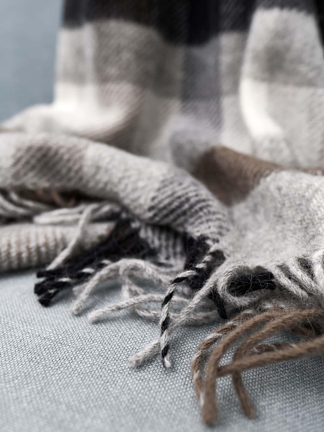 A Gotland Wool Throw – Multi Grey by Klippan with fringes on a couch.