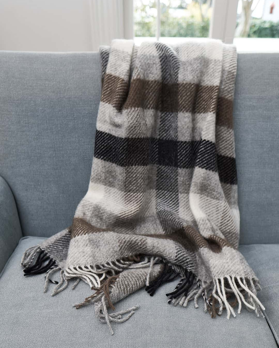 A Gotland Wool Throw – Multi Grey by Klippan on a couch in a living room.
