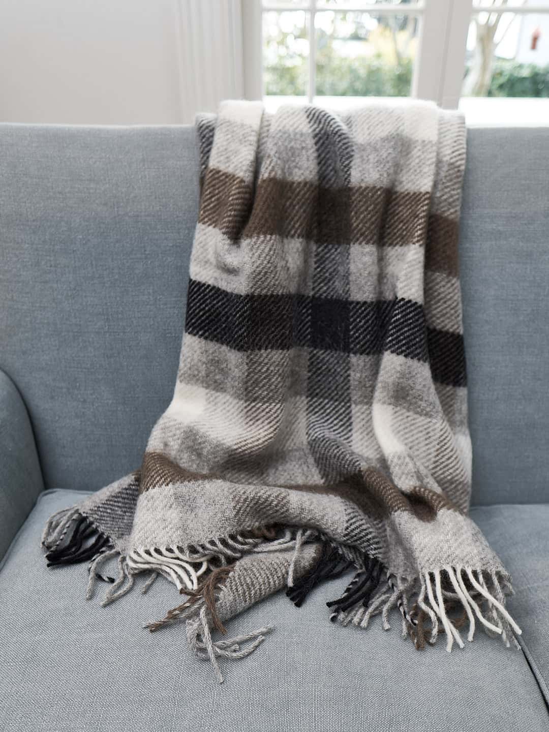 A Gotland Wool Throw – Multi Grey by Klippan on a couch in a living room.