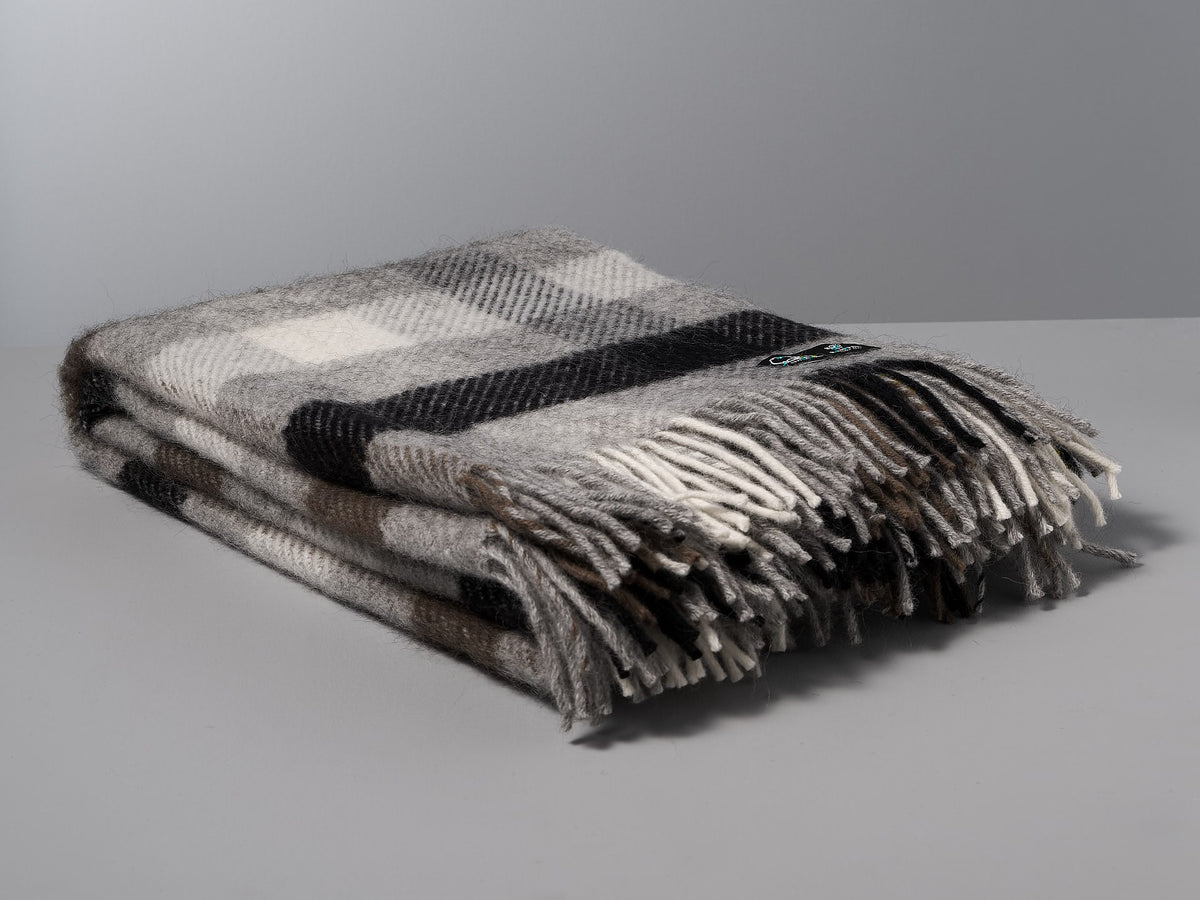 A Klippan Gotland Wool Throw - Multi Grey plaid throw on a grey surface.